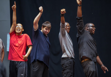 Four young disabled men raise their fists in the air in solidarity