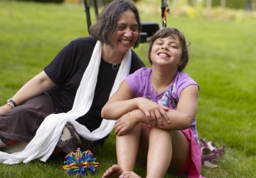 Young girl and a middle aged woman sits in grass field with a walker behind them