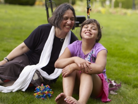 Young girl and a middle aged woman sits in grass field with a walker behind them