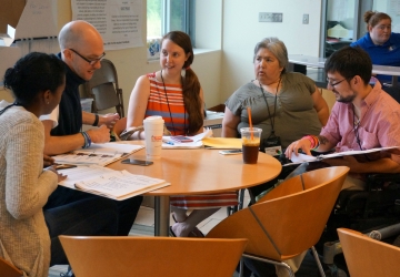 Group of women and male members sitting around a coffee table, discussing plans for an upcoming event