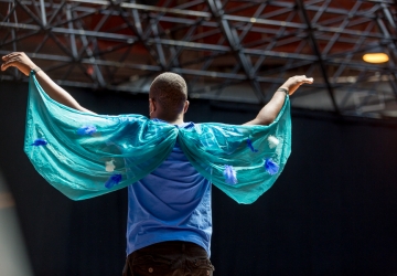 Young man with his back to the camera holds his arms out and slightly above his head, showing off blue fabric wings with stars on them.
