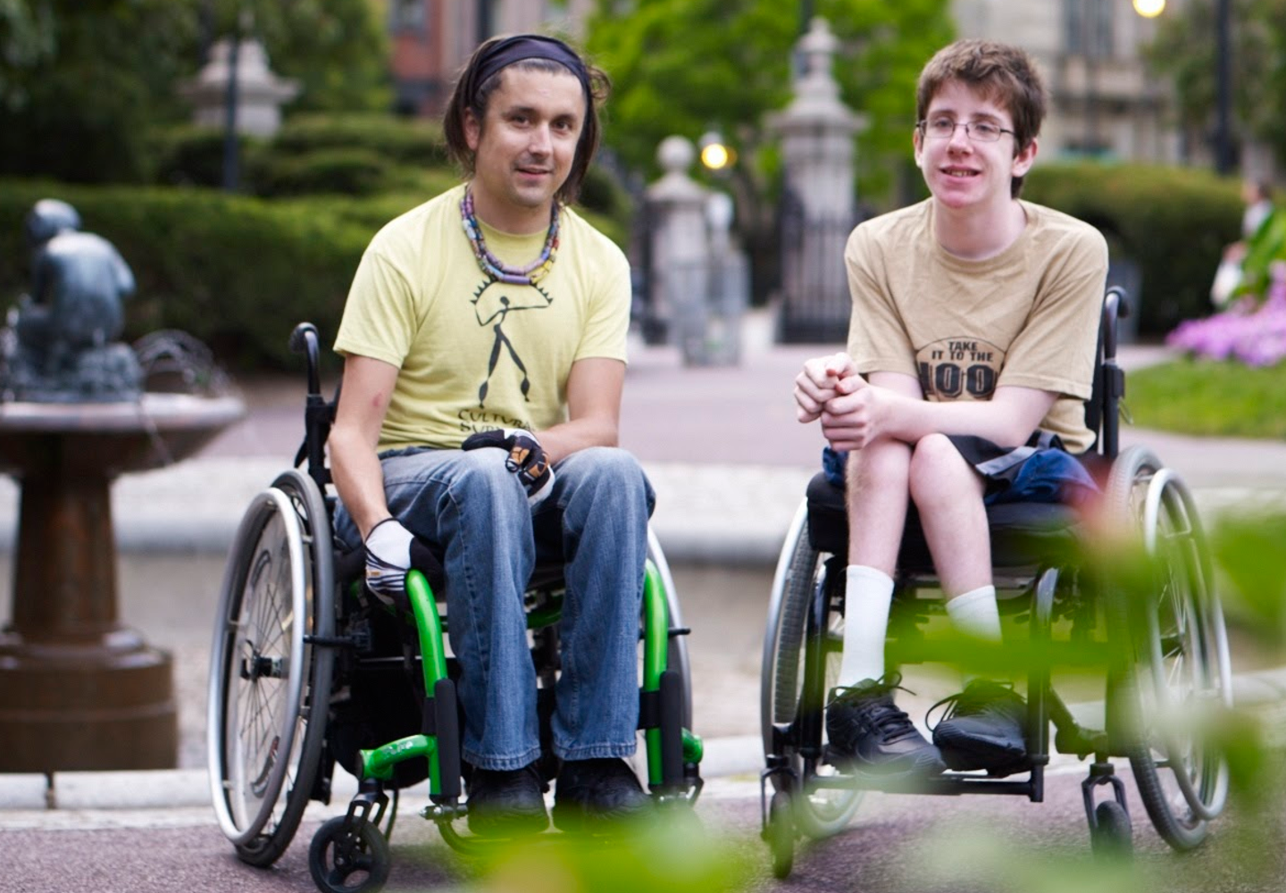 A young man in a wheelchair and a teenage boy in a wheelchair next to each other in the Boston Public Garden.