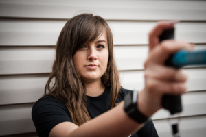 A white deaf woman with long brown hair and wearing a black t-shirt holds a cane horizontally in front of her